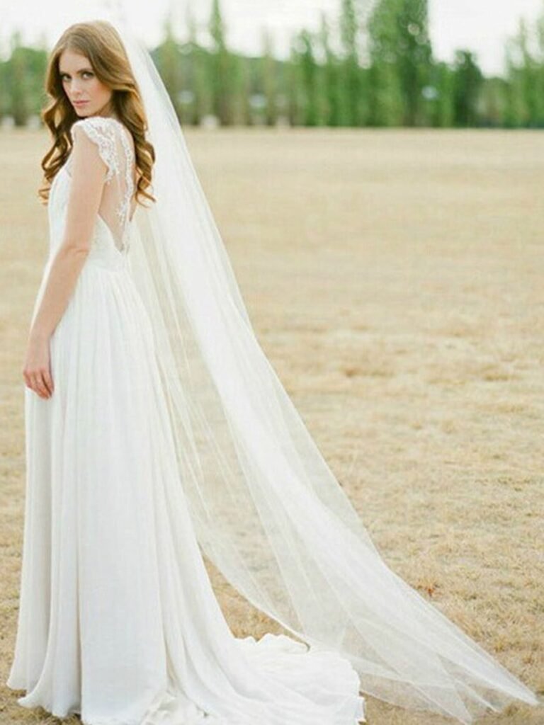 Woman in white wedding dress with long veil, looking over shoulder