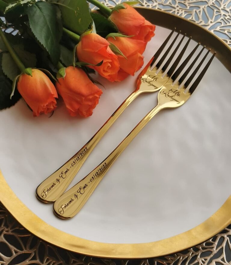 Two engraved gold forks on a plate with orange roses